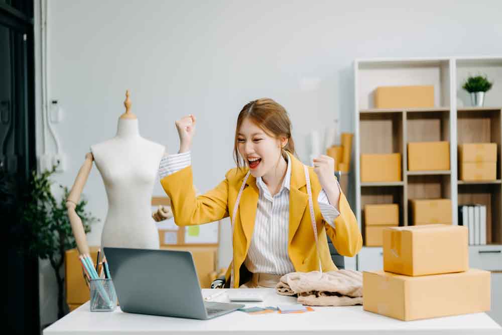 Happy business owner looking at her computer and cheering that her online ads are attracting new customers